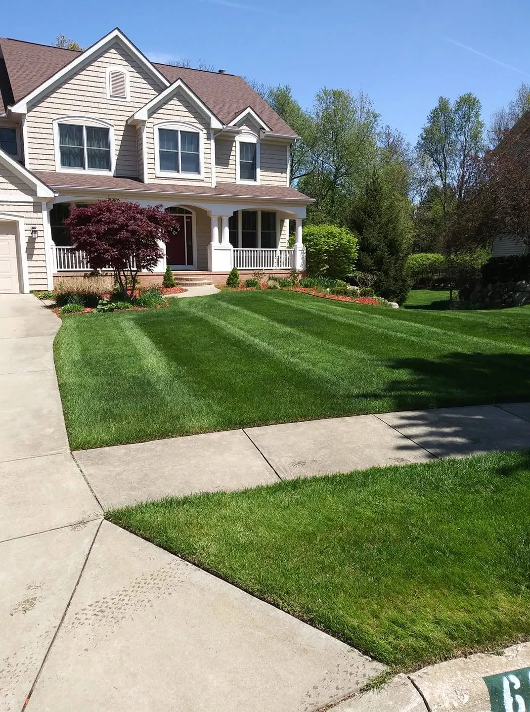 Striped front lawn and fresh mulch beds at a two-story shingled home with a covered porch